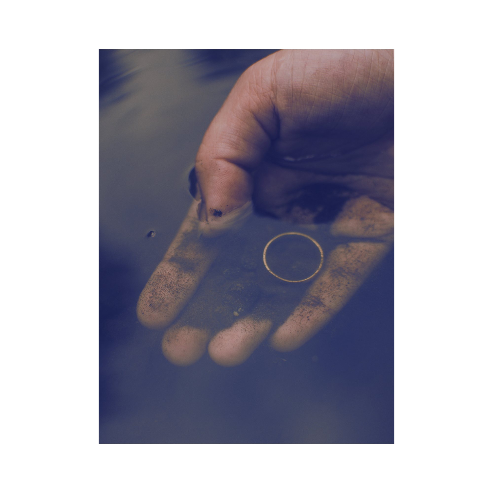 A hand held just beneath still water, a thin gold ring resting in the palm, almost hidden below the surface